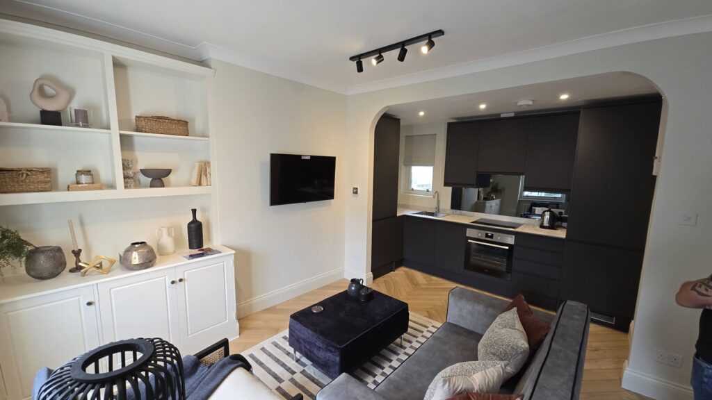 Dark fitted kitchen and white living-room shelving in a refurbished Paddington flat